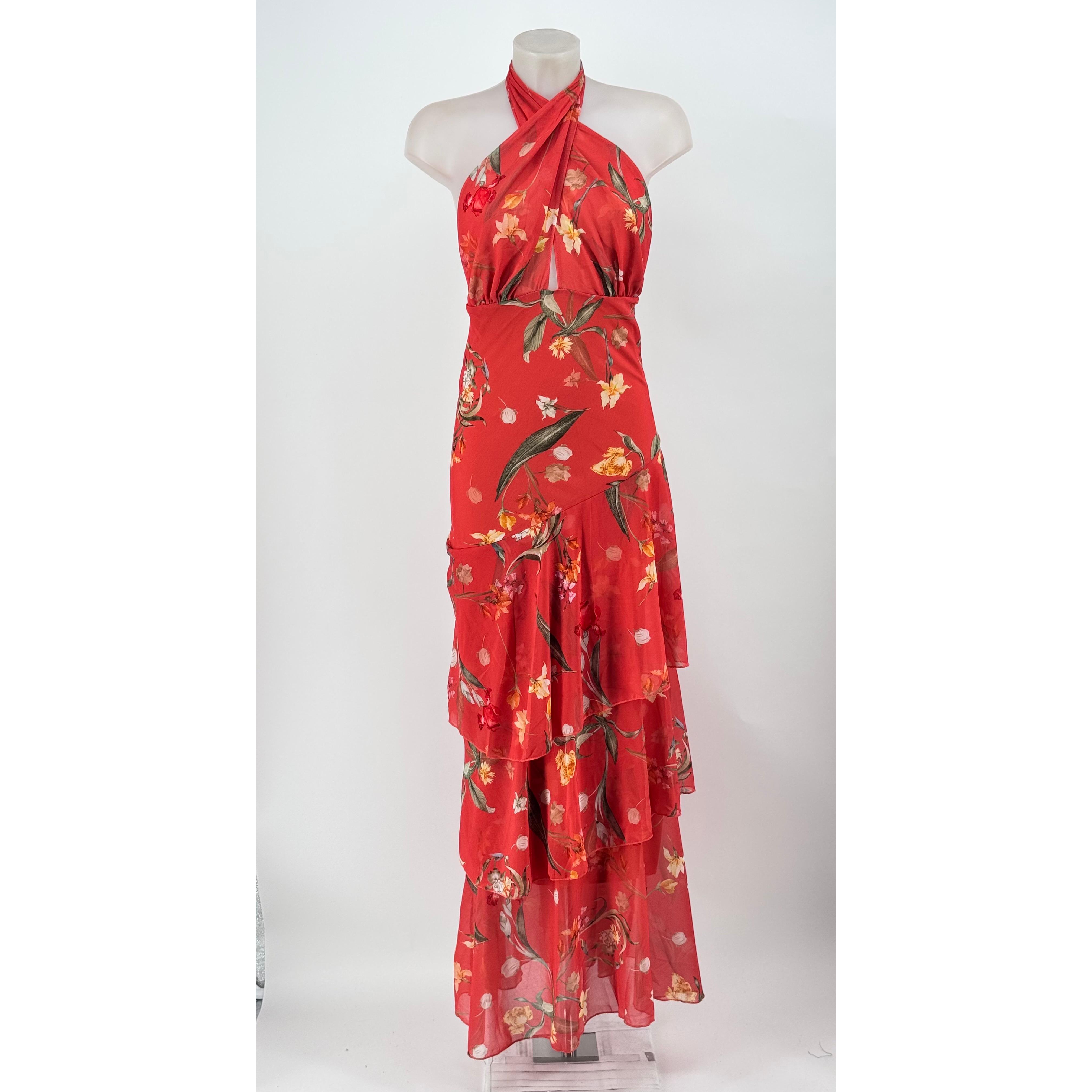 Vestido largo de fiesta en fluido tejido chiffon con deslumbrante estampado floral. Presenta un sofisticado escote halter cruzado al cuello con lazo posterior, espalda totalmente descubierta y una elegante falda de vuelo con cascada de volantes.