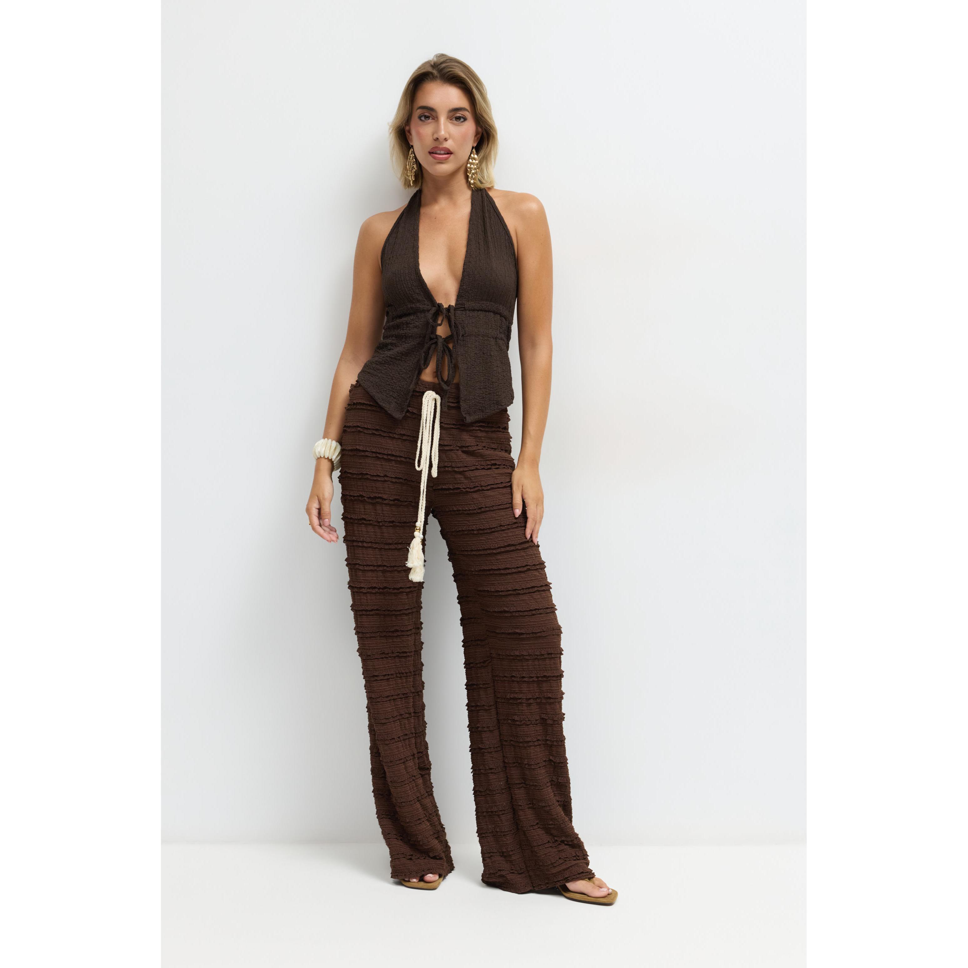 Pantalón fluido de mujer en tejido de licra elástico con textura de minivolantes horizontales. Corte de pata ancha estilo palazzo, cintura elástica y cordón ajustador con borlas y cuentas. Disponible en varios colores ideales para un look boho chic único.